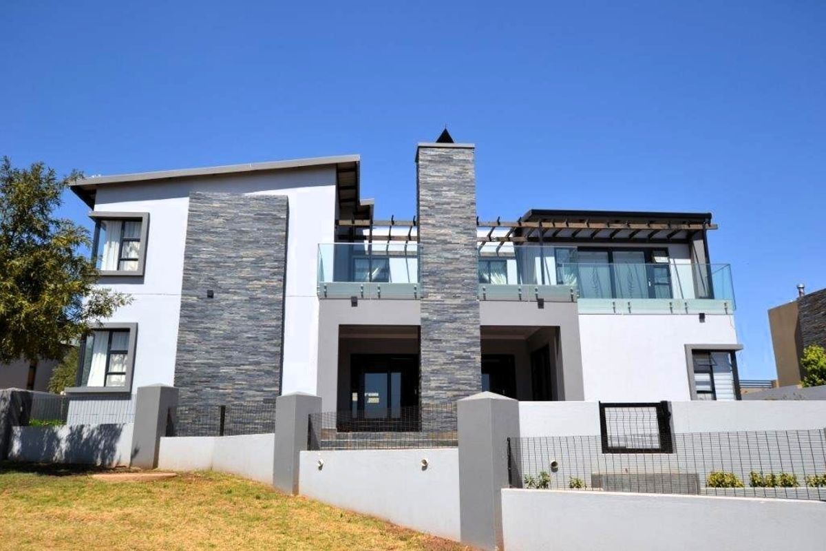 Modern double-story residence featuring stone cladding, glass balustrades, and a timber pergola over the rear patio area.
