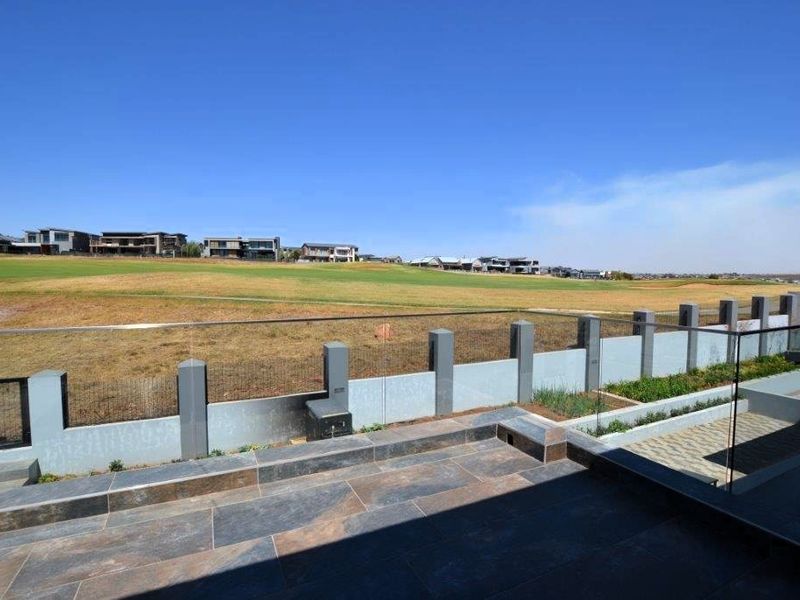 A modern outdoor patio featuring stone tile flooring, a sleek glass balustrade, and raised garden beds, overlooking an expansive estate landscape.