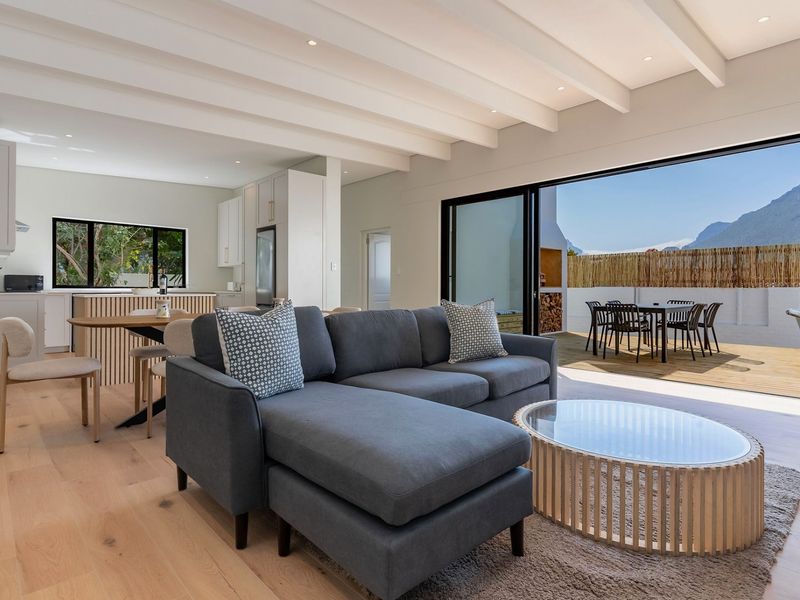 Modern open-plan living and kitchen area featuring exposed beam ceilings, light hardwood floors, and large sliding doors opening to an outdoor patio.