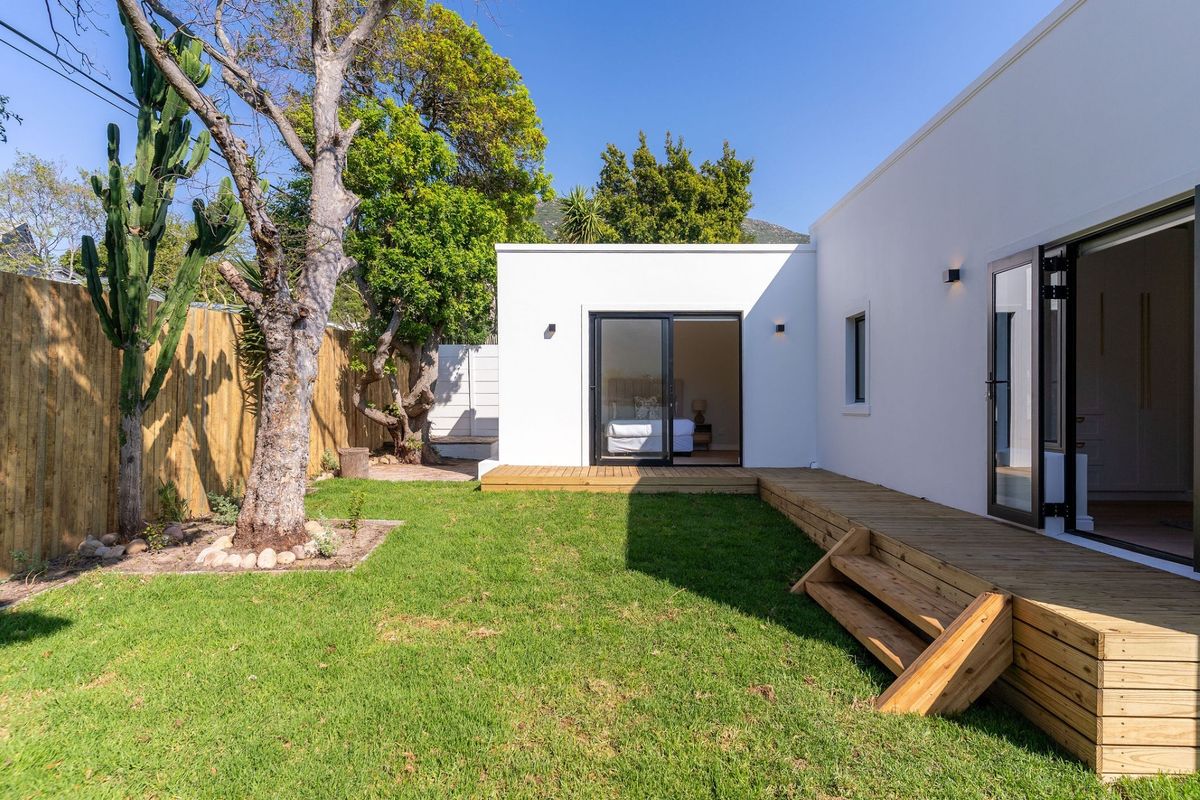 A well-maintained rear garden featuring a timber deck, lush lawn, and modern sliding glass doors providing seamless indoor-outdoor flow.