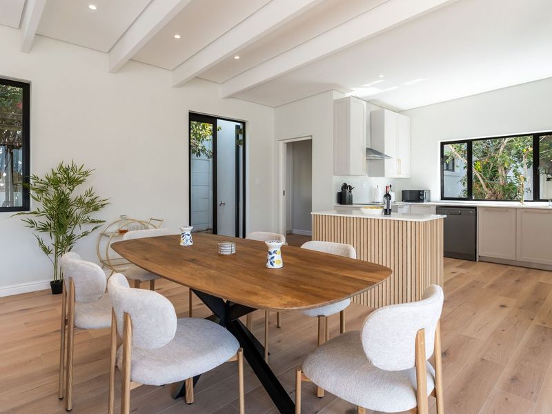 A bright open-plan living and dining area featuring timber flooring, exposed ceiling beams, and a modern kitchen with a slatted timber island.