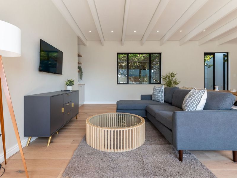 A bright and modern living room featuring exposed beam ceilings, timber flooring, and large black-framed windows that provide natural light.