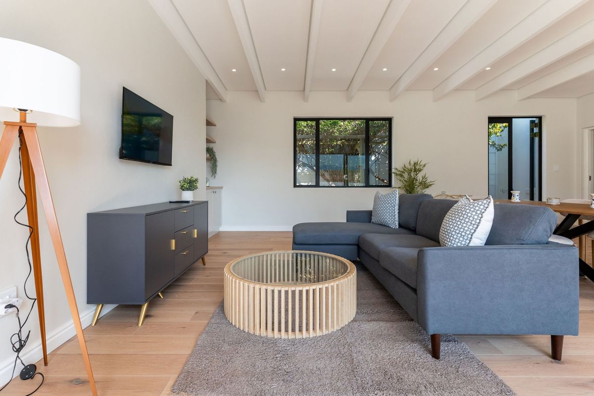 A bright and modern living room featuring exposed beam ceilings, timber flooring, and large black-framed windows that provide natural light.