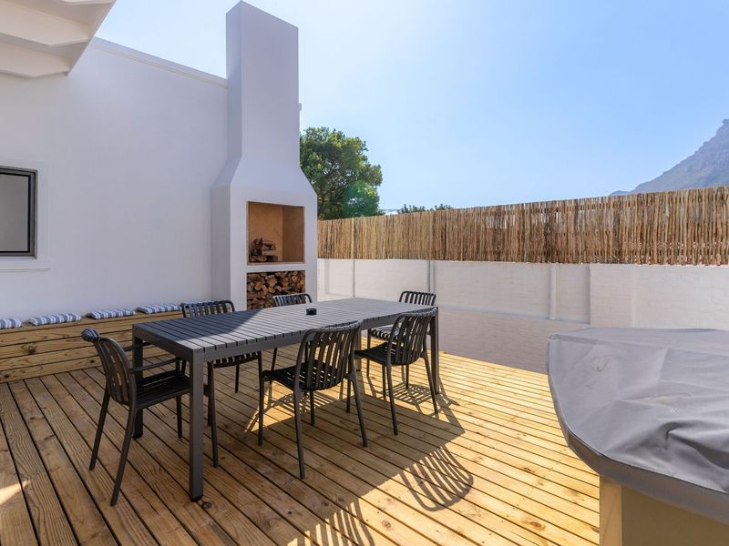 A well-maintained outdoor patio featuring timber decking, a built-in fireplace, and integrated bench seating, enclosed by a privacy fence.