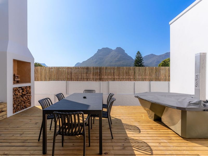 A spacious outdoor patio featuring timber decking, a built-in fireplace, and scenic mountain views, perfect for alfresco dining and entertaining.