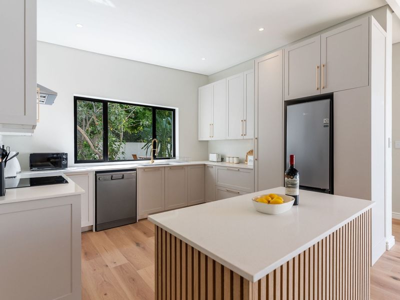 Modern, high-end kitchen featuring light shaker-style cabinetry, quartz countertops, a central island with timber detailing, and premium integrated fixtures.
