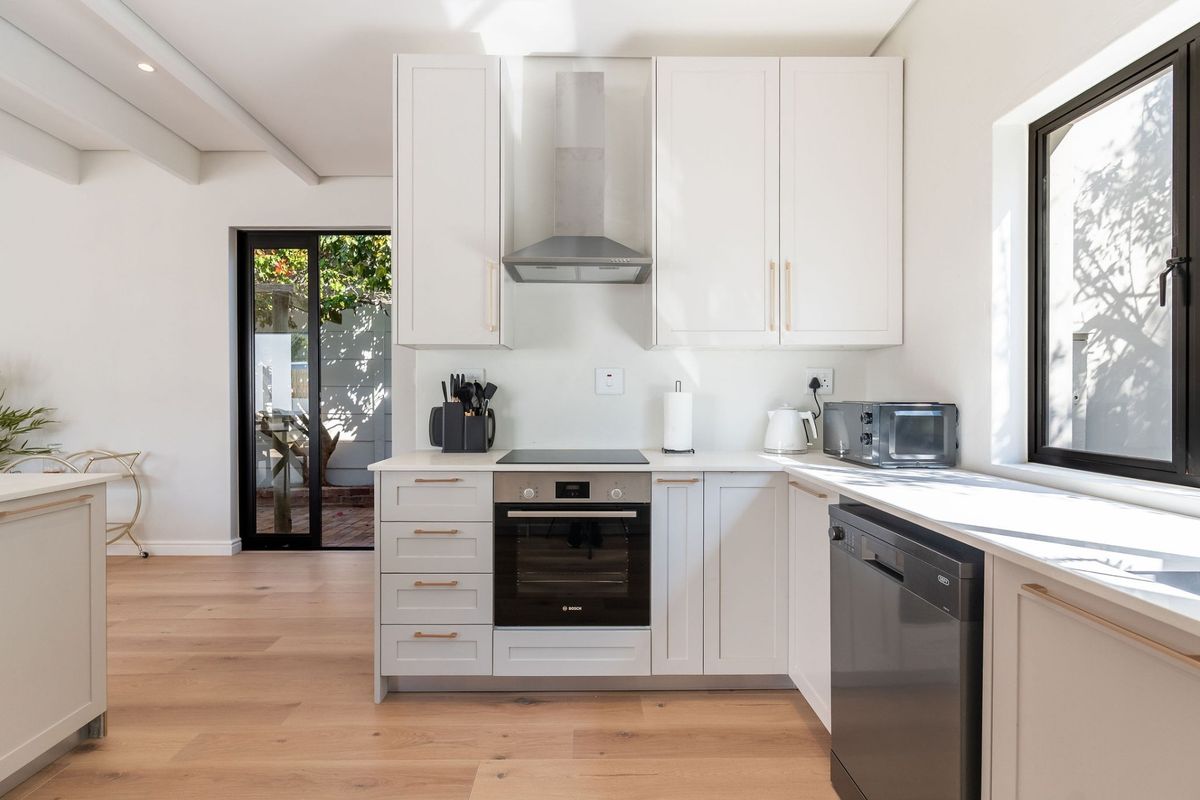 Modern kitchen featuring white cabinetry, integrated appliances, electric hob, oven, and light timber flooring with direct access to an outdoor patio area.