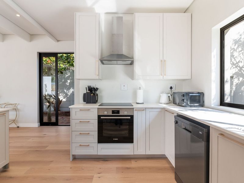 Modern kitchen featuring white cabinetry, integrated appliances, electric hob, oven, and light timber flooring with direct access to an outdoor patio area.