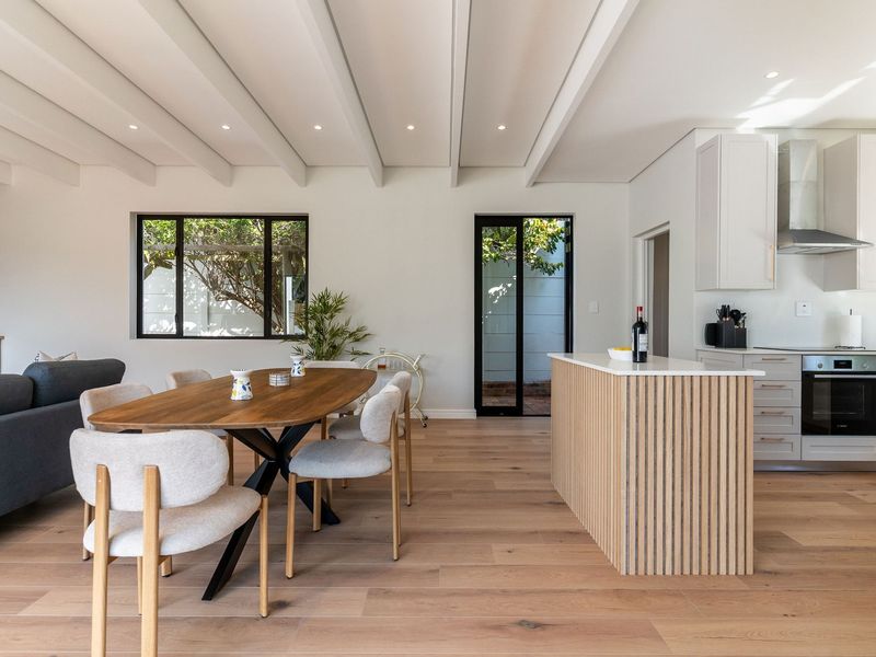 Modern open-plan living and dining area featuring exposed beam ceilings, timber flooring, and a contemporary kitchen with a slatted island and integrated appliances.