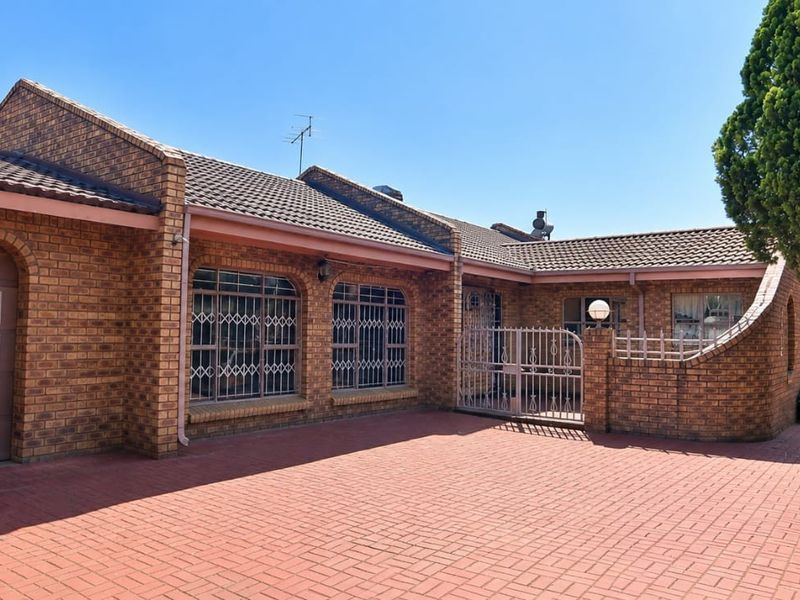 Front elevation of a face brick house featuring a paved driveway, integrated garage, and secure gated entrance.