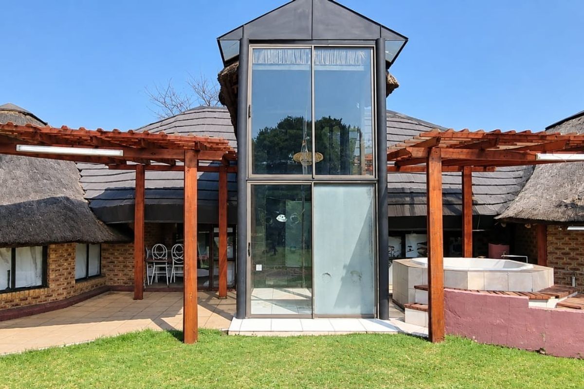 Rear exterior view featuring a unique glass tower entrance, thatched roof sections, a timber pergola, and a built-in spa on a tiled patio area.