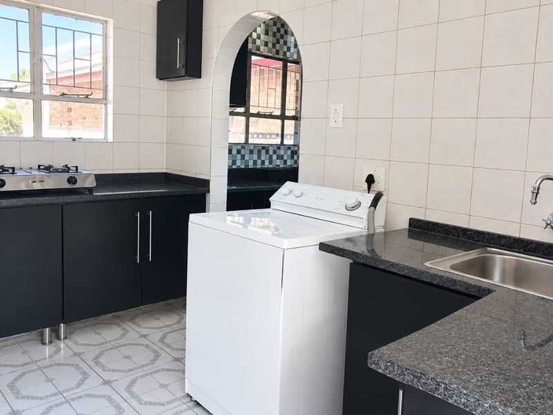 Functional kitchen featuring dark cabinetry, granite countertops, stainless steel sink, and a gas hob, with an arched doorway leading to a secondary utility area.
