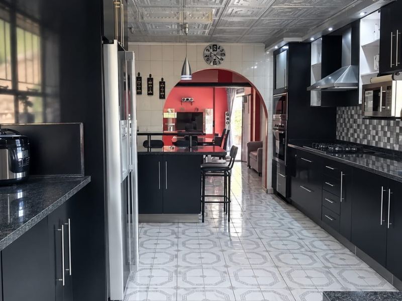 Modern kitchen featuring dark cabinetry, granite countertops, integrated appliances, and a tiled backsplash, leading through an archway into the living area.