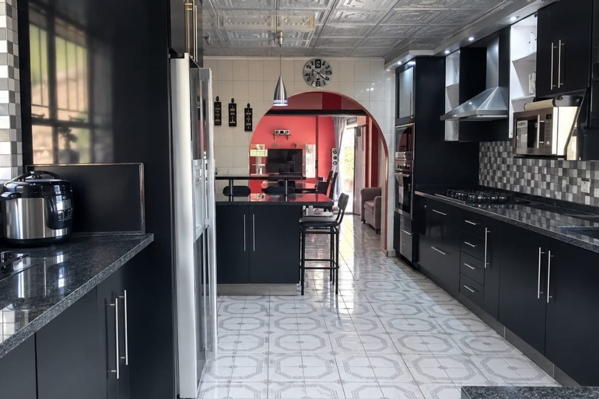 Modern kitchen featuring dark cabinetry, granite countertops, integrated appliances, and a tiled backsplash, leading through an archway into the living area.