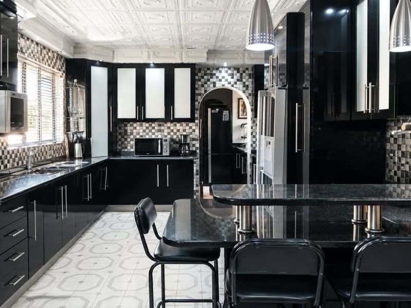 Modern kitchen featuring high-gloss black cabinetry, granite countertops, mosaic tile backsplash, and a unique decorative coffered ceiling with a breakfast bar.