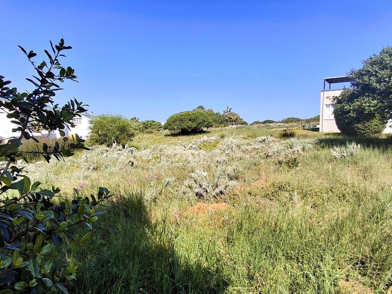 A view of a vacant residential plot featuring natural vegetation and sloped terrain, situated between existing neighboring properties.
