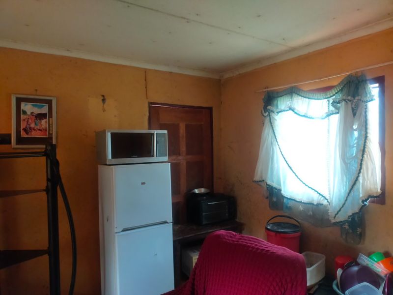 A small kitchen area featuring basic wall finishes and a window, currently showing significant signs of wear and requiring cosmetic updates.