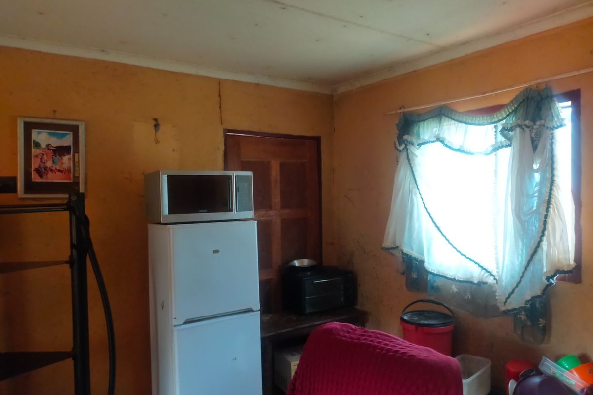 A small kitchen area featuring basic wall finishes and a window, currently showing significant signs of wear and requiring cosmetic updates.