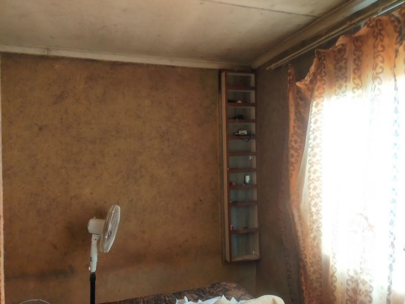 A bedroom featuring a built-in shelving unit, currently showing significant wear and staining on the wall and ceiling surfaces.
