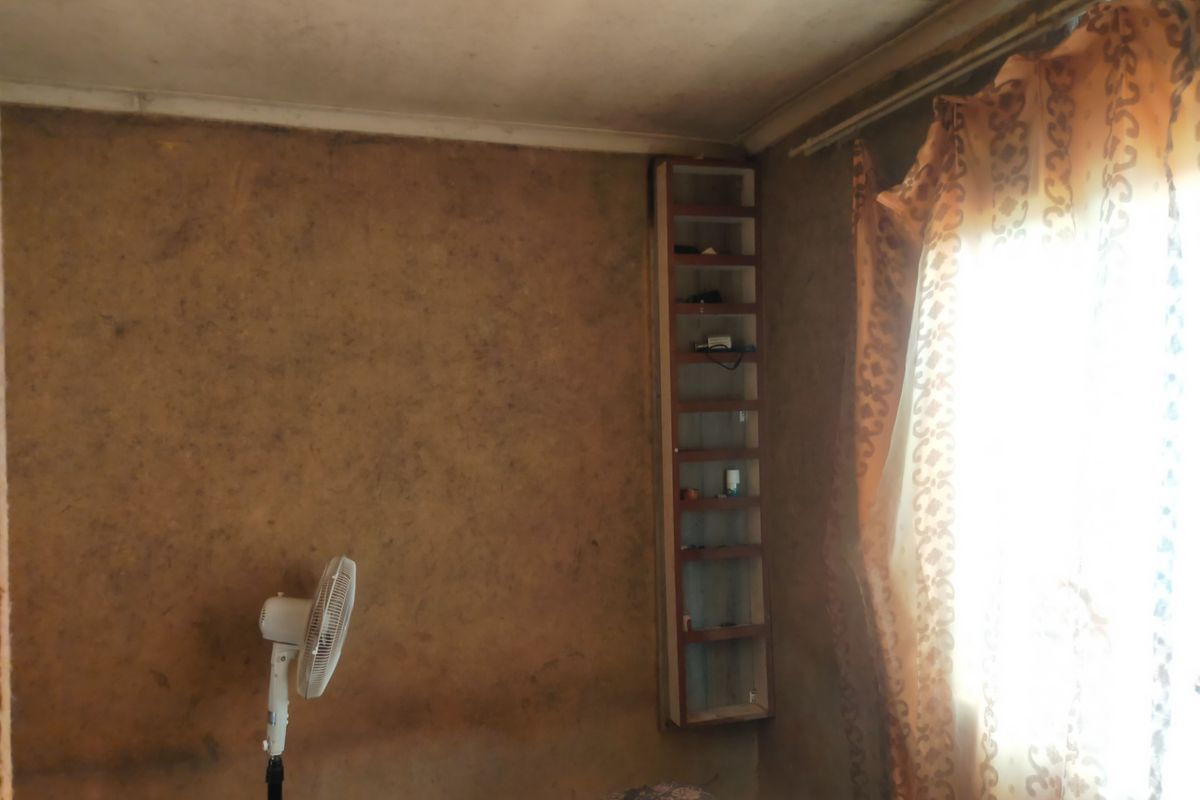 A bedroom featuring a built-in shelving unit, currently showing significant wear and staining on the wall and ceiling surfaces.
