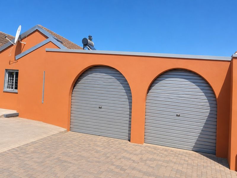 Exterior view of a double garage featuring arched roller doors, paved driveway, and a solar water heating system mounted on the roof.