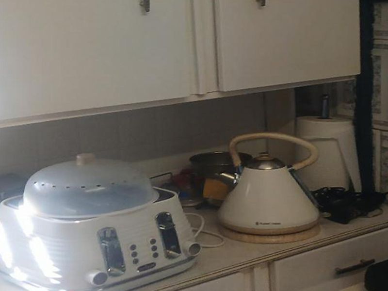 A close-up view of a dated kitchen workspace featuring laminate countertops, tiled backsplash, and traditional cabinetry.
