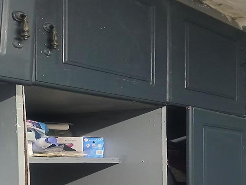 Close-up view of dark-painted kitchen cabinetry showing signs of wear and peeling ceiling paint, indicating a need for refurbishment.
