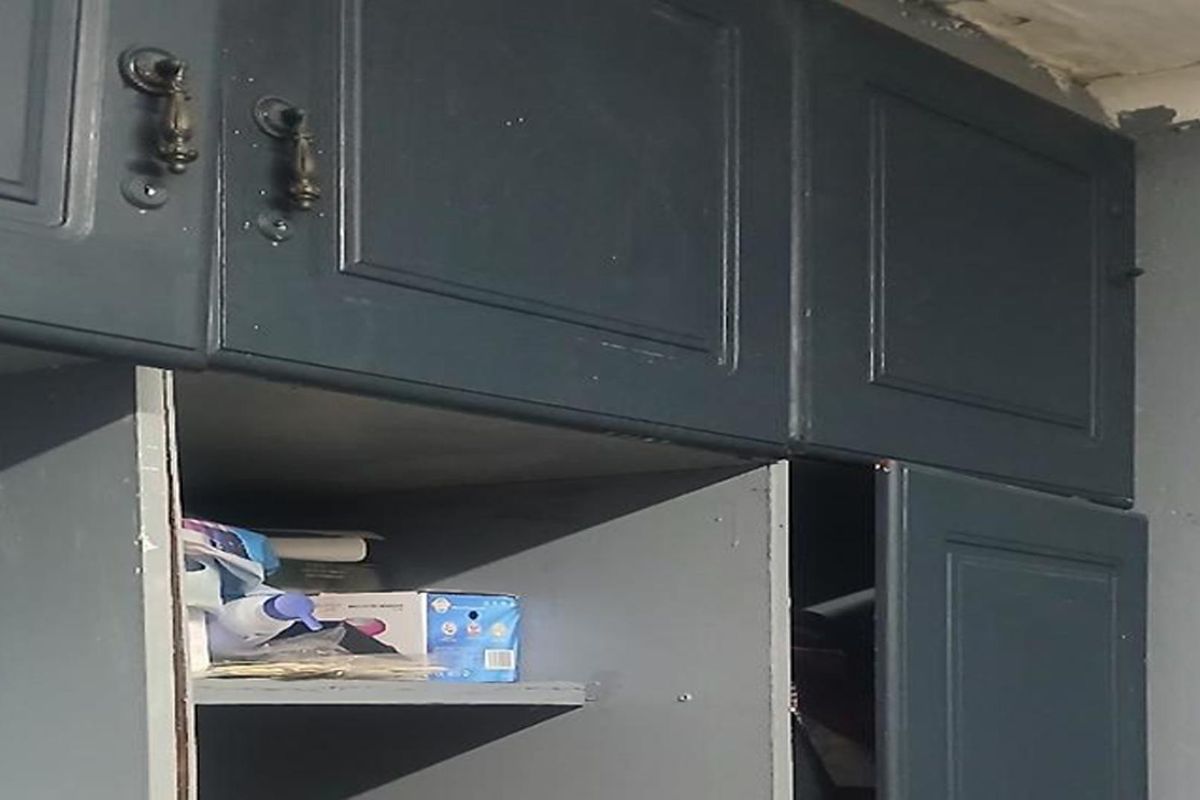Close-up view of dark-painted kitchen cabinetry showing signs of wear and peeling ceiling paint, indicating a need for refurbishment.