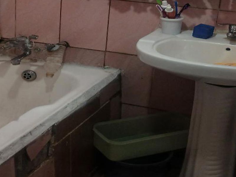 A dated bathroom featuring a pedestal basin and bathtub with pink wall tiling, showing significant signs of wear and requiring renovation.