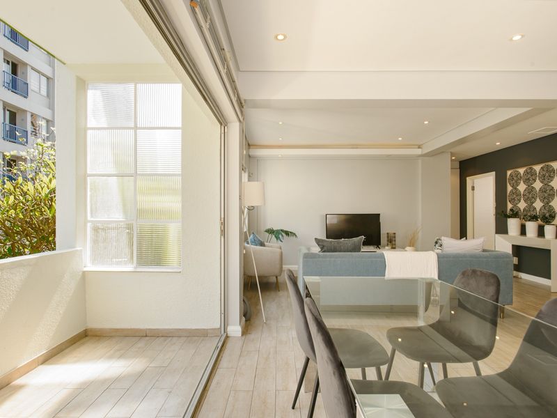 Bright open-plan living and dining area featuring modern tiled flooring, recessed lighting, and seamless access to a private balcony through large sliding glass doors.