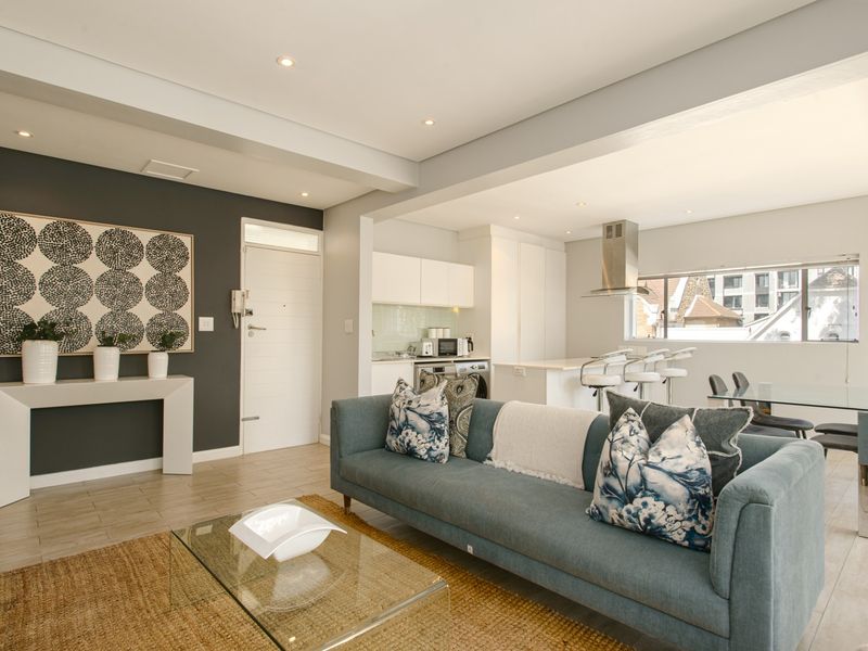 Modern open-plan living area featuring a sleek kitchen with island, recessed lighting, and neutral tiled flooring, creating a bright and functional space.