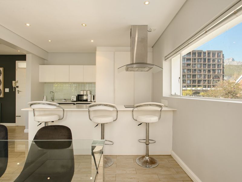 Modern open-plan kitchen featuring sleek white cabinetry, a central island with breakfast bar, and integrated stainless steel extractor fan, complemented by neutral tiled flooring.