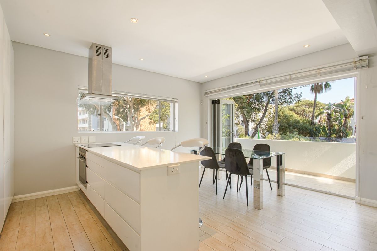 Modern open-plan kitchen and dining area featuring a sleek island, built-in appliances, and large sliding doors opening onto a private balcony.