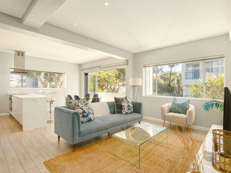 Bright open-plan living area featuring a modern kitchen with island, built-in appliances, and seamless flow to a balcony through large sliding glass doors.