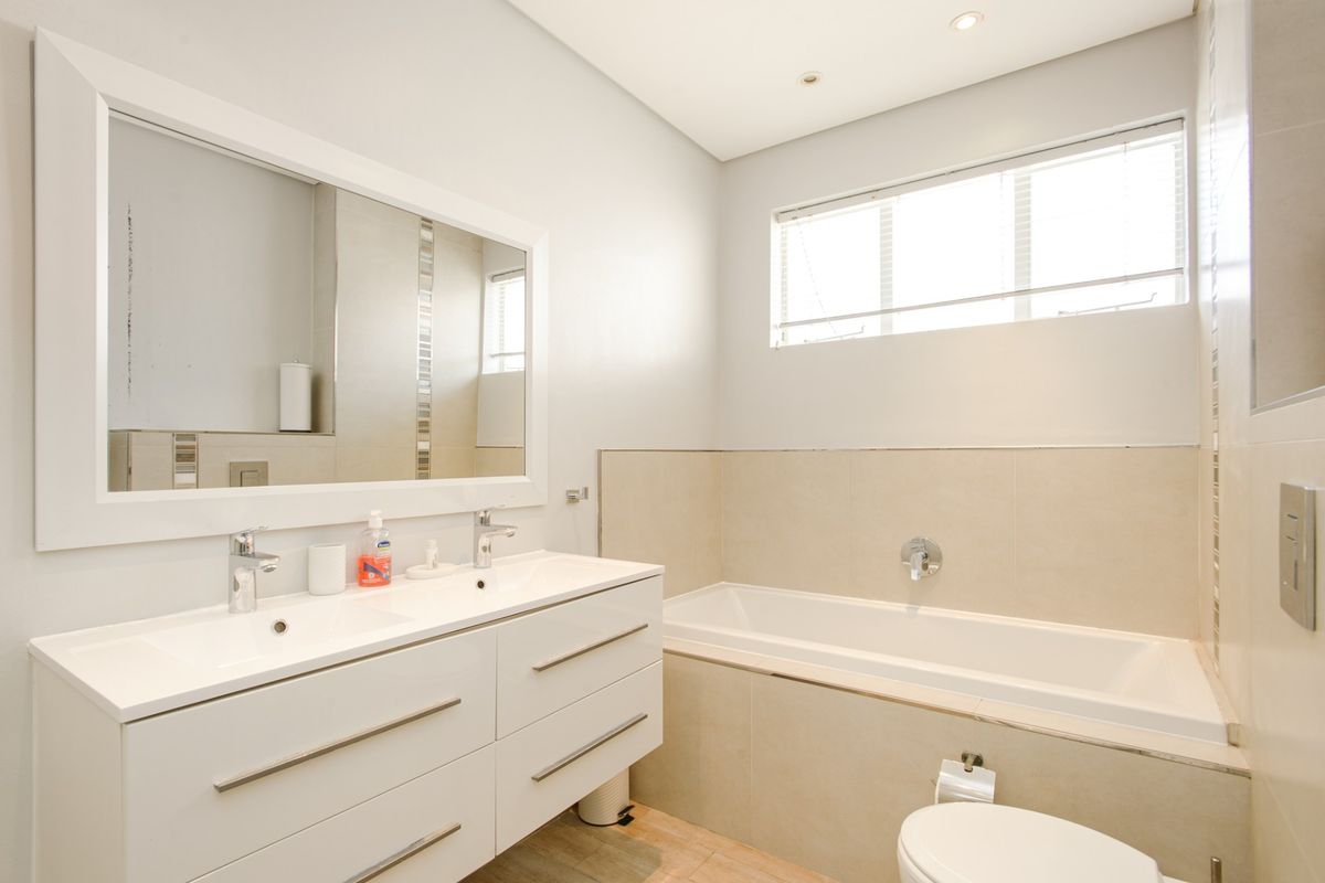 Modern bathroom featuring a double vanity, built-in bathtub, wall-mounted toilet, and neutral tiling throughout.