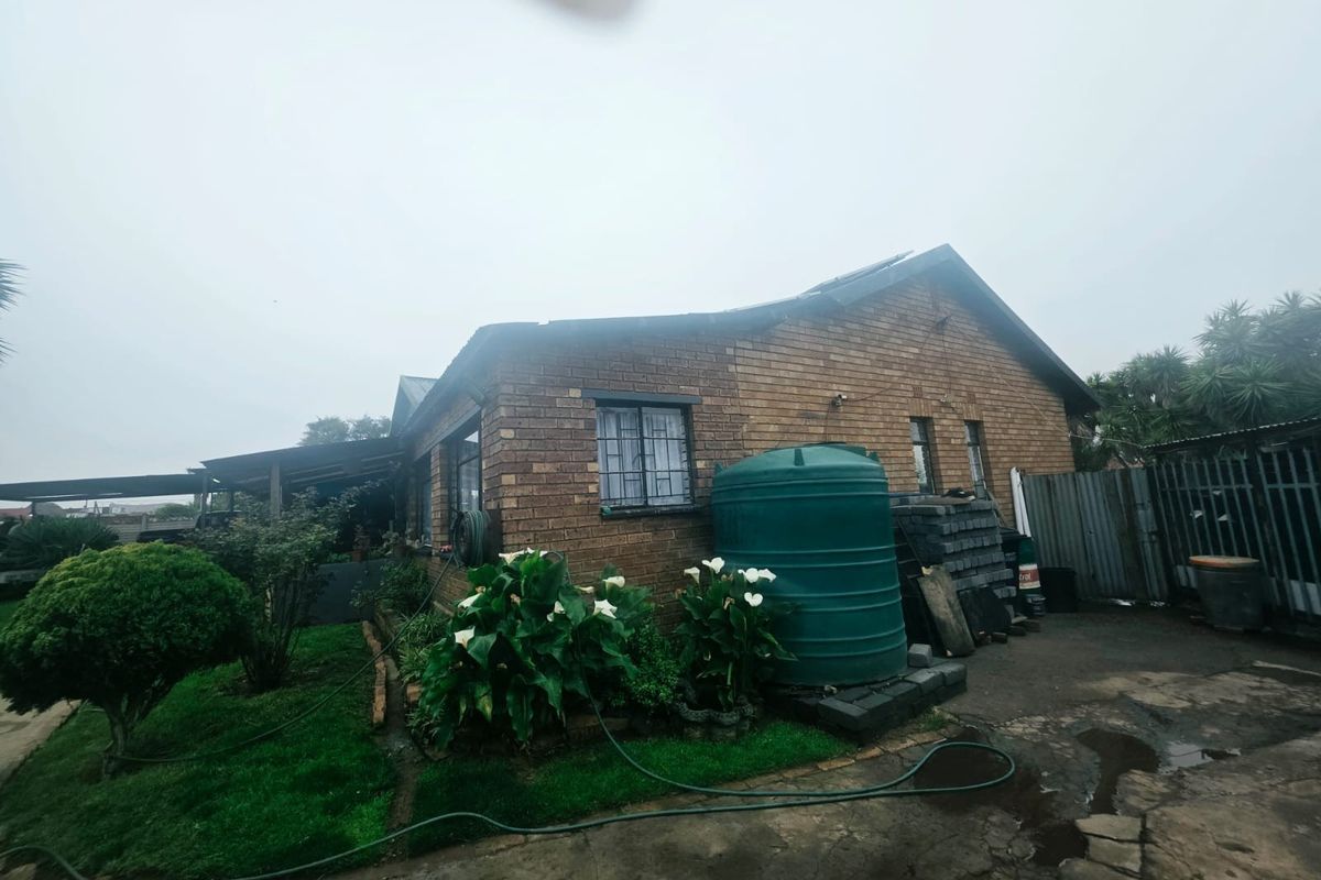 Rear view of a face brick house featuring a water storage tank, security bars on windows, and a paved outdoor area.