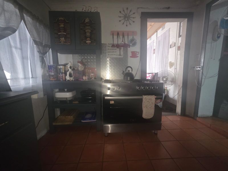 A functional kitchen area featuring a freestanding gas stove, tiled flooring, and a metal splashback, providing a practical cooking space.