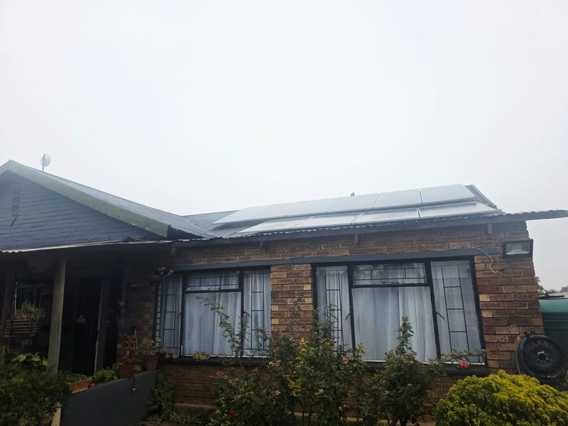 Front elevation of a brick house featuring a corrugated metal roof equipped with solar panels and security-barred windows.