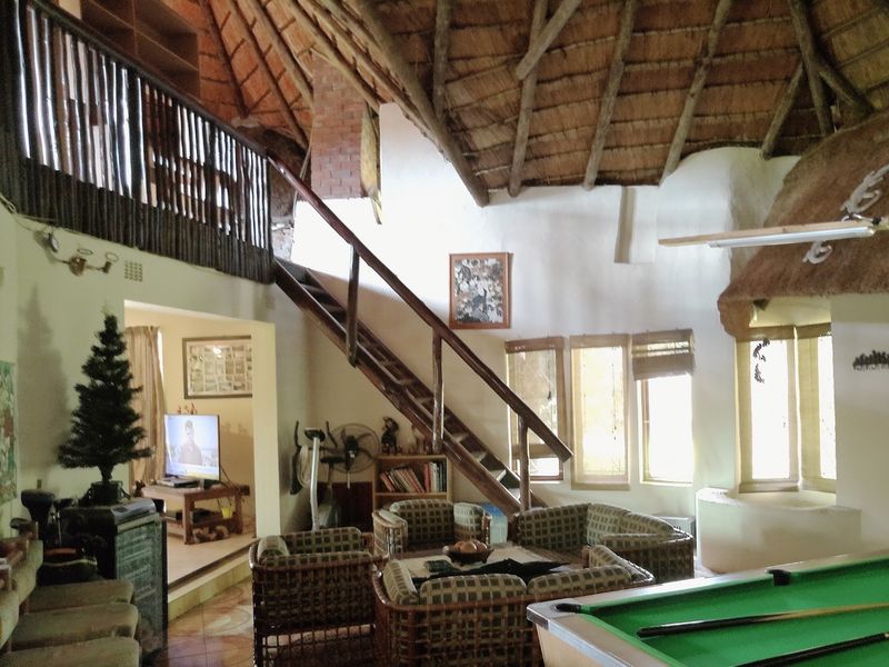 Spacious living area featuring a high thatched roof with exposed timber rafters, a mezzanine level, and a central timber staircase.
