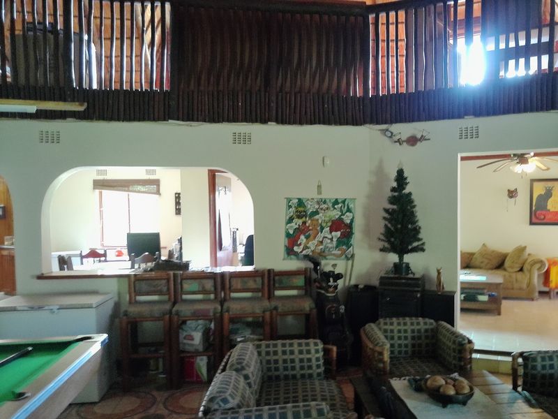 Open plan living area featuring a mezzanine level with wooden railing, arched architectural openings, and tiled flooring throughout the connected spaces.