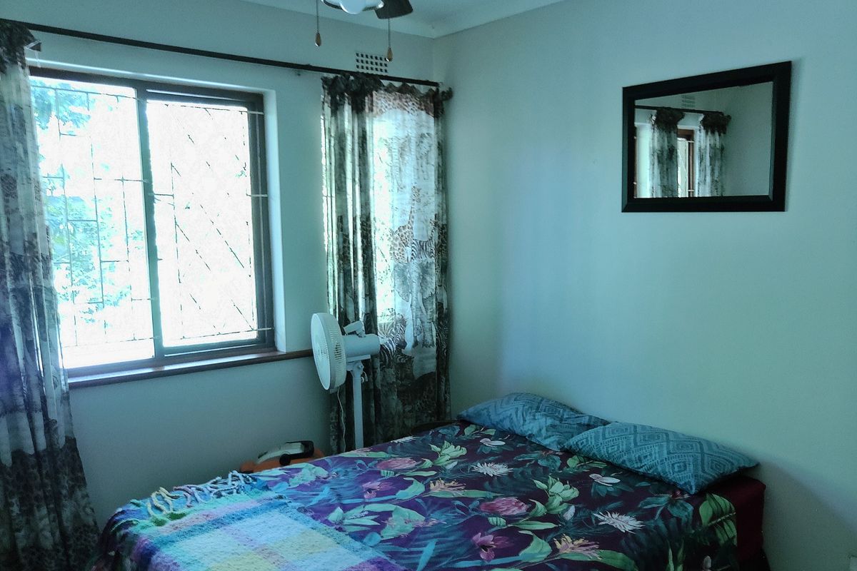 A standard bedroom featuring a ceiling fan, sliding window with security bars, and neutral wall finishes.