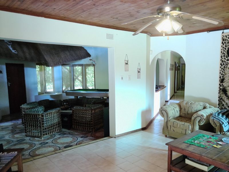Open plan living area featuring tiled flooring, a timber ceiling with a central fan, and an arched transition to the hallway.