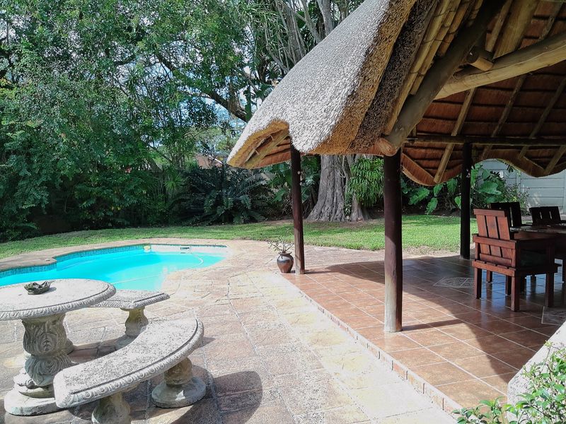 Outdoor entertainment area featuring a swimming pool, stone-paved surround, and a covered thatched lapa with tiled flooring.