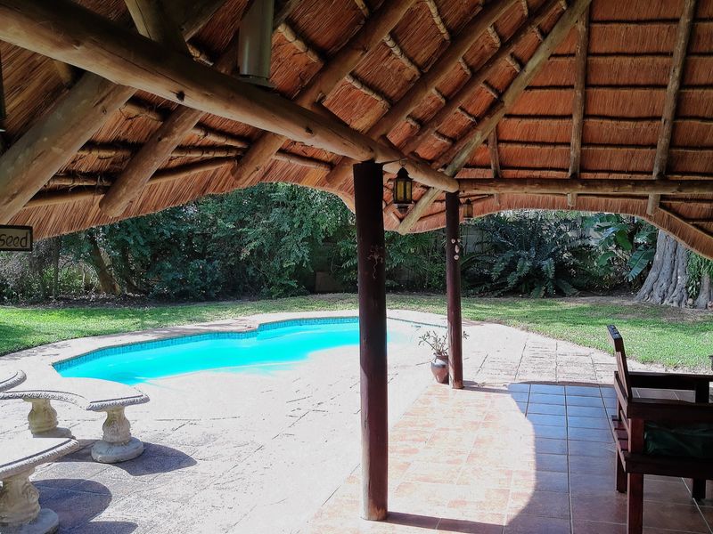 Outdoor entertainment area featuring a thatched lapa overlooking a swimming pool with paved surround and established garden.