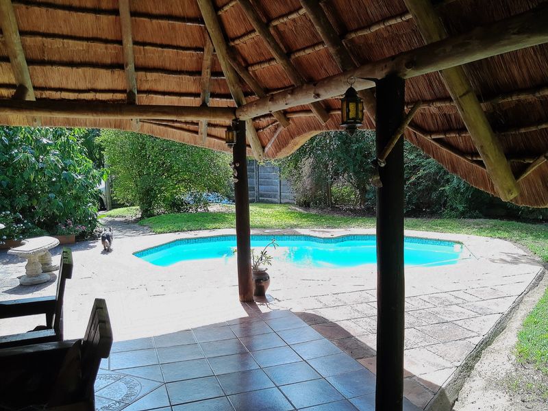 Covered outdoor patio with a traditional thatch roof overlooking a private swimming pool and landscaped garden area.