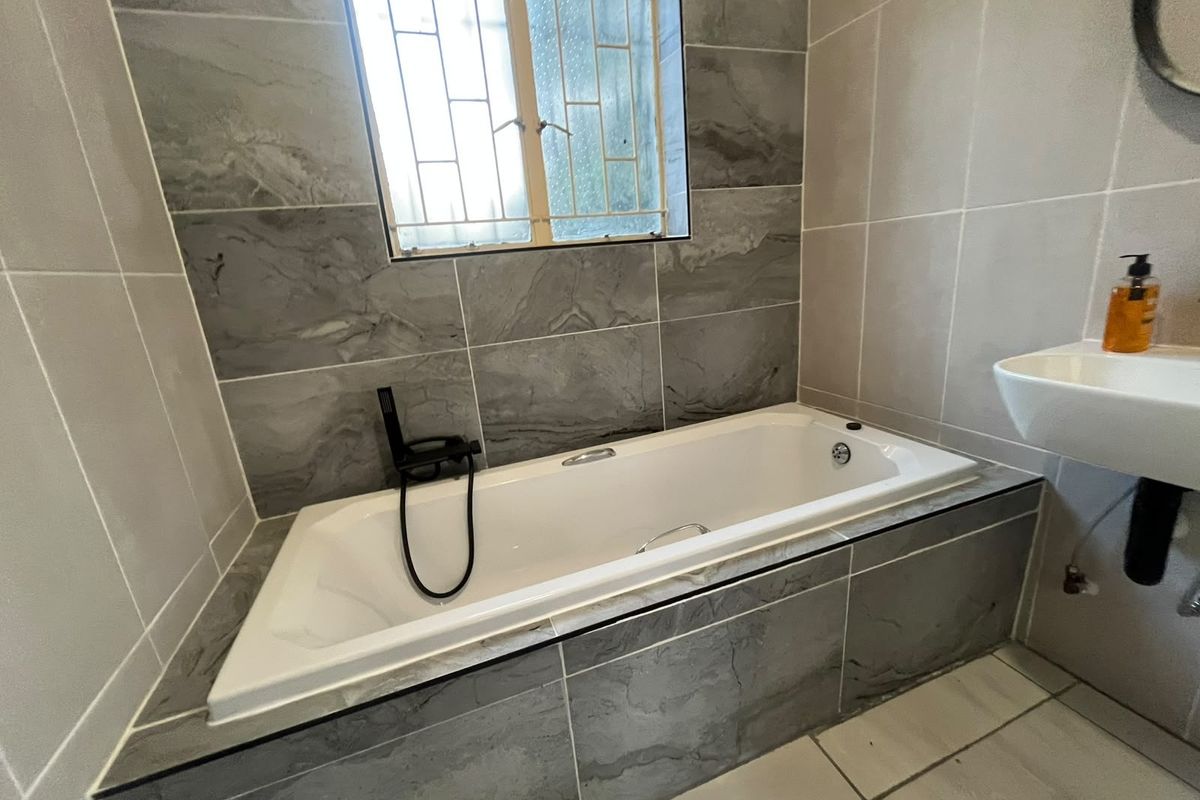 A modern bathroom featuring a built-in bathtub with contemporary black fixtures and neutral grey wall tiling.