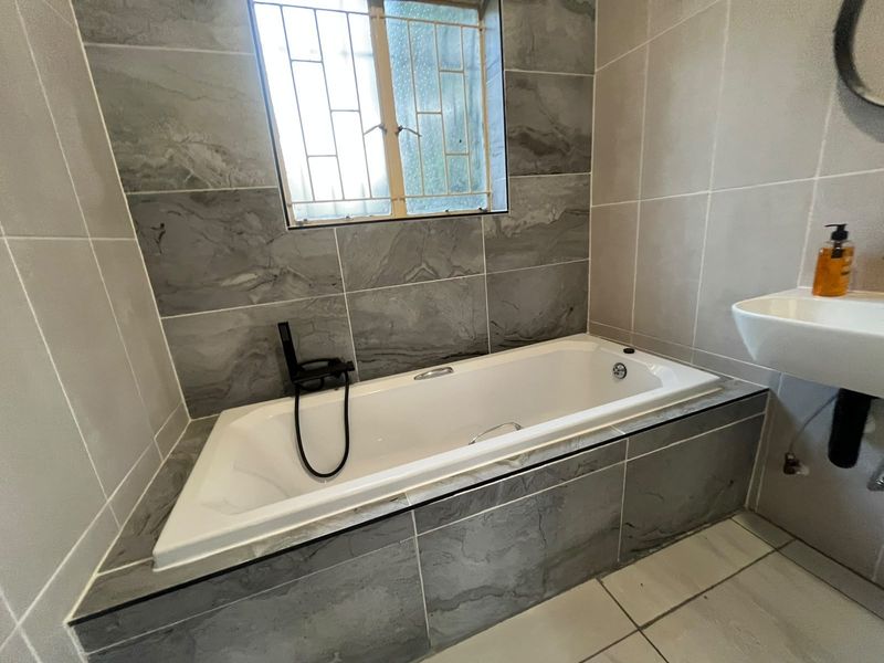 A modern bathroom featuring a built-in bathtub with contemporary black fixtures and neutral grey wall tiling.