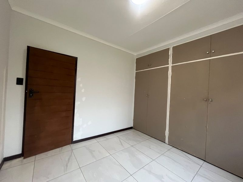 A vacant bedroom featuring neutral tiled flooring and built-in storage cupboards, ready for personalization and minor cosmetic updates.