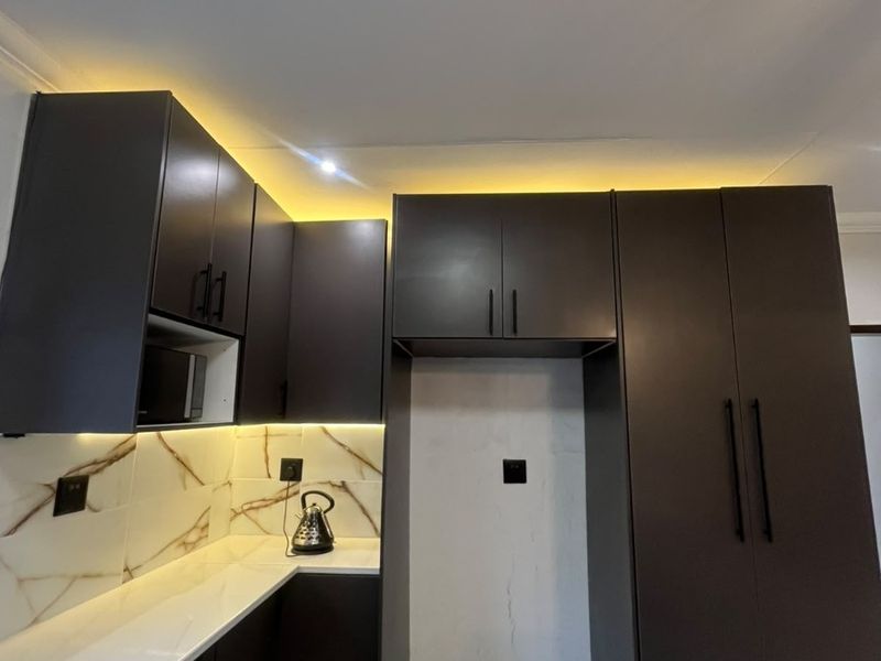 Modern kitchen featuring dark matte cabinetry, white stone countertops, marble-look backsplash, and integrated under-cabinet lighting.