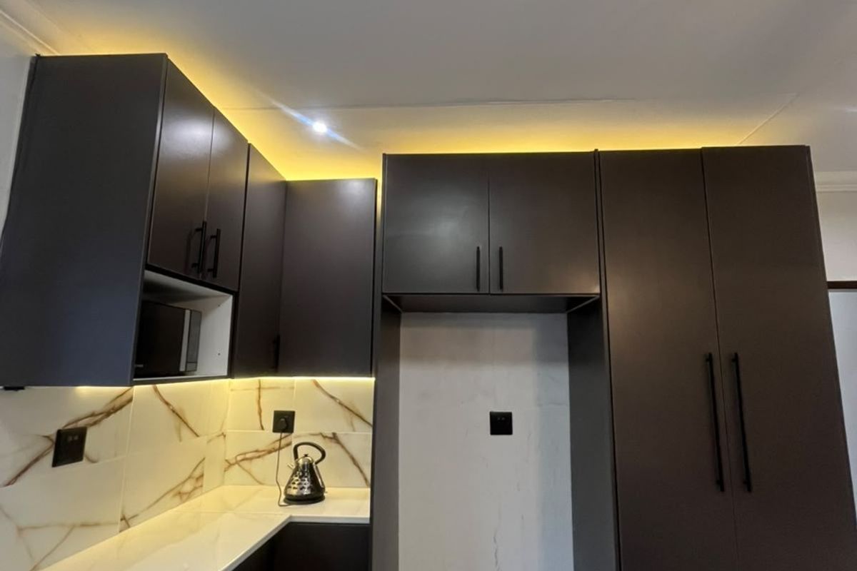 Modern kitchen featuring dark matte cabinetry, white stone countertops, marble-look backsplash, and integrated under-cabinet lighting.